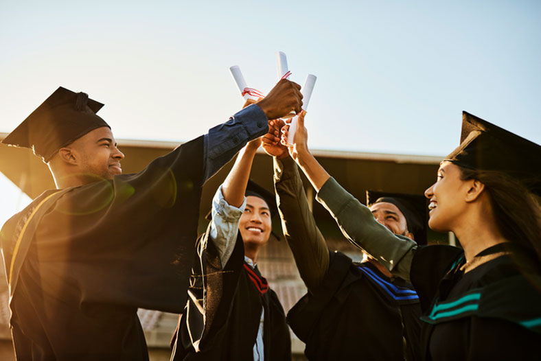 recent graduates holding diplomas in the air